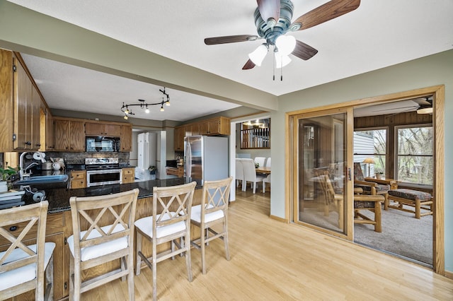 kitchen featuring stainless steel appliances, light wood-style floors, dark countertops, a sink, and a peninsula