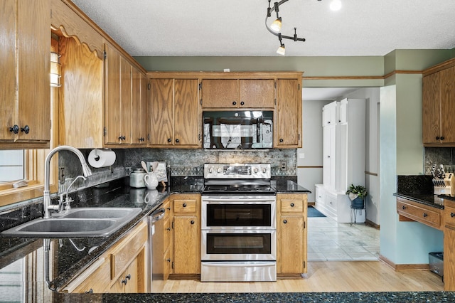 kitchen with light wood finished floors, a sink, stainless steel appliances, decorative backsplash, and brown cabinetry