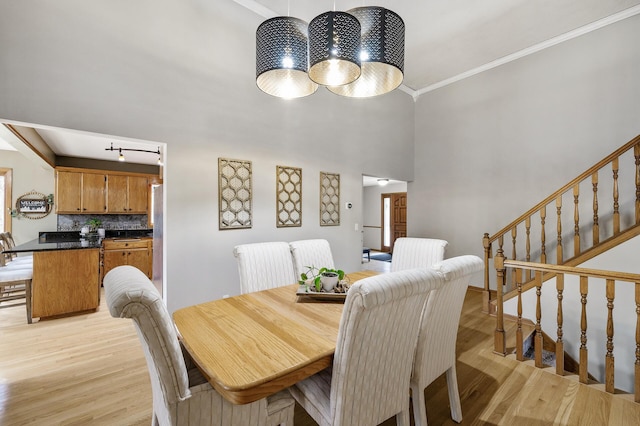 dining room featuring crown molding, light wood finished floors, stairs, and an inviting chandelier