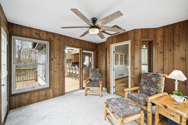 living area with wooden walls, a ceiling fan, visible vents, and carpet
