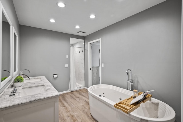 bathroom with a shower stall, a sink, double vanity, a freestanding tub, and wood finished floors