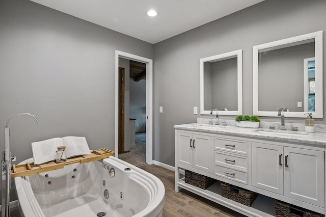 full bathroom with double vanity, wood finished floors, a jetted tub, and a sink