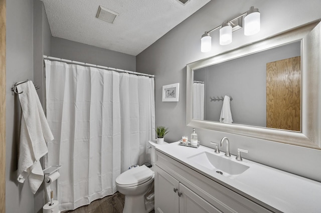 bathroom with vanity, toilet, visible vents, a textured ceiling, and wood finished floors