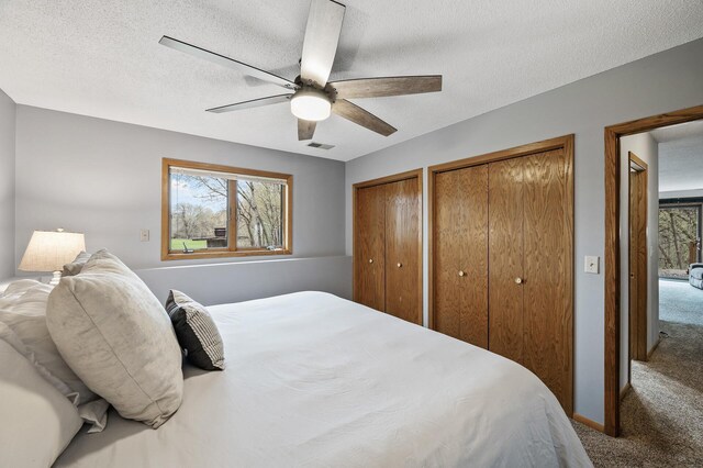 carpeted bedroom with visible vents, ceiling fan, a textured ceiling, and multiple closets