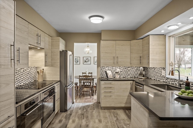 kitchen featuring light brown cabinets, dark countertops, a sink, backsplash, and stainless steel appliances