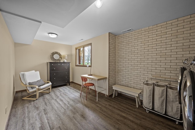 sitting room featuring visible vents, baseboards, wood finished floors, and brick wall
