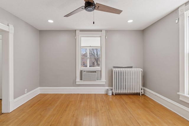unfurnished room with a ceiling fan, light wood finished floors, baseboards, and radiator