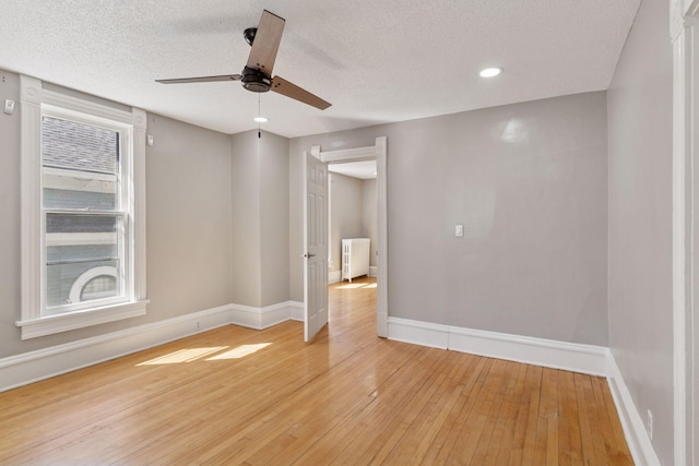spare room with radiator heating unit, light wood-type flooring, a ceiling fan, and baseboards