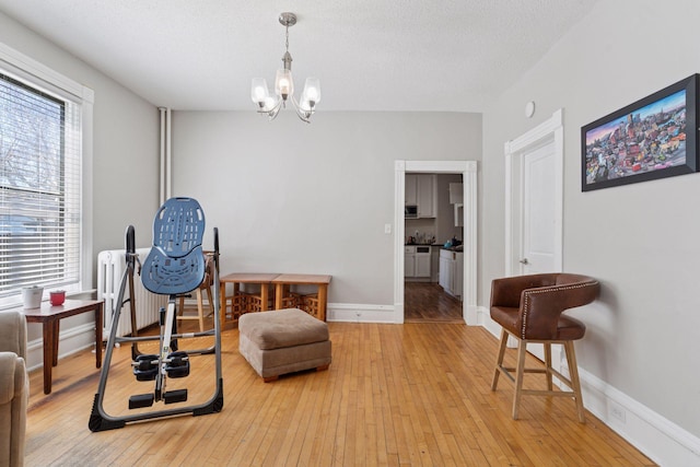living area with a chandelier, baseboards, a textured ceiling, and light wood-style flooring