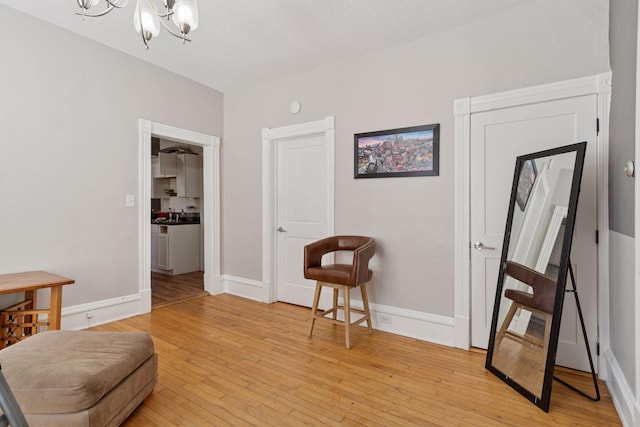 living area featuring an inviting chandelier, a textured ceiling, light wood-style flooring, and baseboards