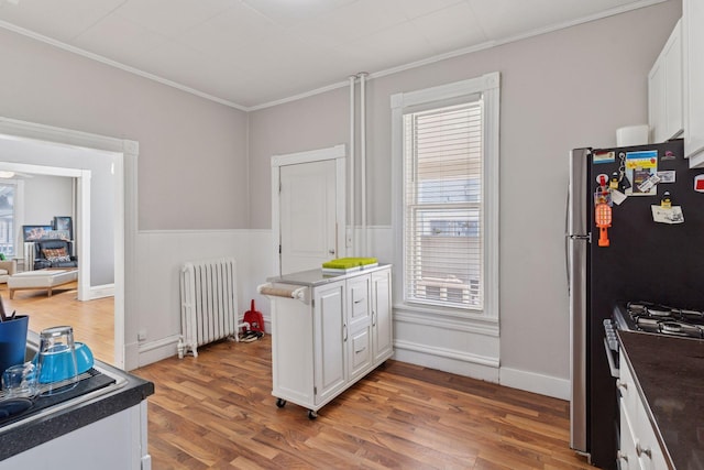 kitchen featuring white cabinetry, stainless steel gas range oven, radiator, and ornamental molding