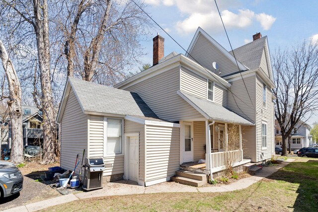 view of front of property featuring a porch, roof with shingles, and a chimney