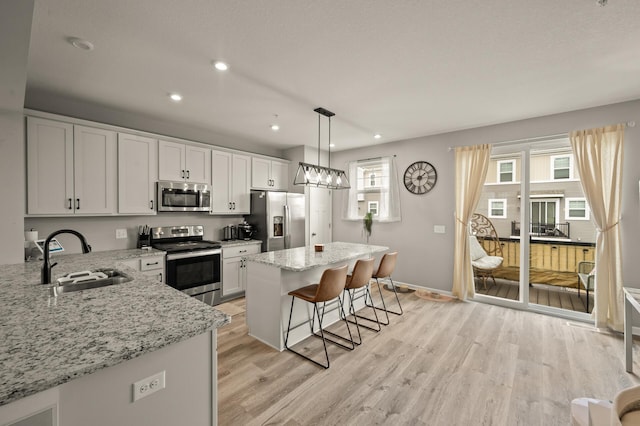 kitchen with light wood-style floors, a kitchen breakfast bar, a center island, appliances with stainless steel finishes, and a sink