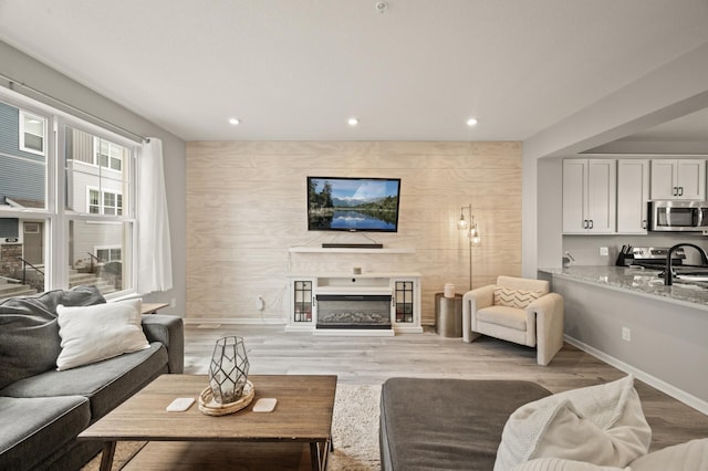 living room featuring baseboards, recessed lighting, a glass covered fireplace, and light wood-style floors