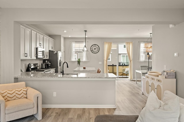 kitchen featuring white cabinets, a sink, a peninsula, light wood-style floors, and stainless steel appliances