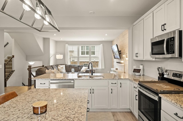 kitchen featuring open floor plan, white cabinetry, light stone countertops, stainless steel appliances, and a sink