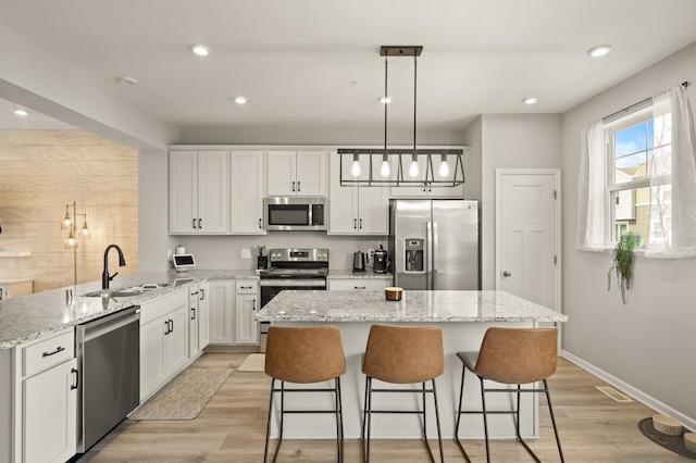 kitchen with a peninsula, white cabinetry, a kitchen island, appliances with stainless steel finishes, and a sink