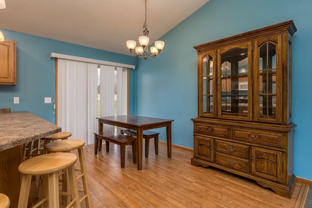 dining area with light wood-type flooring, vaulted ceiling, baseboards, a chandelier, and a textured ceiling