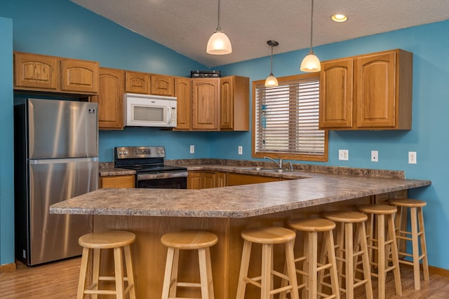 kitchen featuring a peninsula, a textured ceiling, lofted ceiling, stainless steel appliances, and a sink