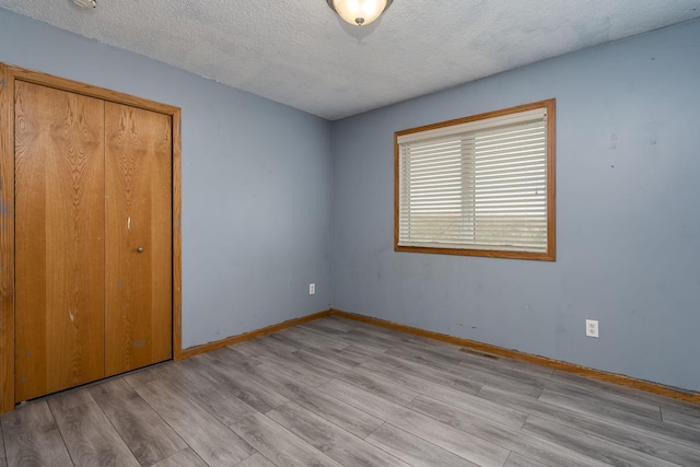 unfurnished bedroom with light wood-style flooring, a textured ceiling, a closet, visible vents, and baseboards