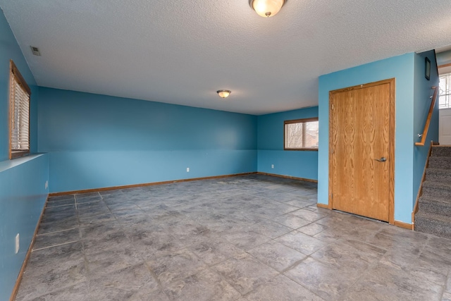 unfurnished room featuring stairs, a textured ceiling, baseboards, and a healthy amount of sunlight