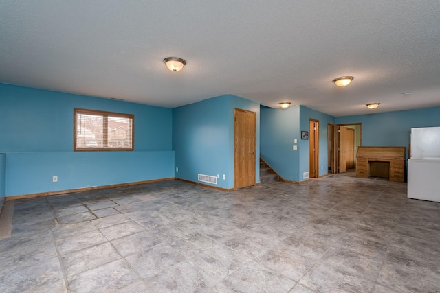 unfurnished living room featuring visible vents, baseboards, stairway, and a textured ceiling