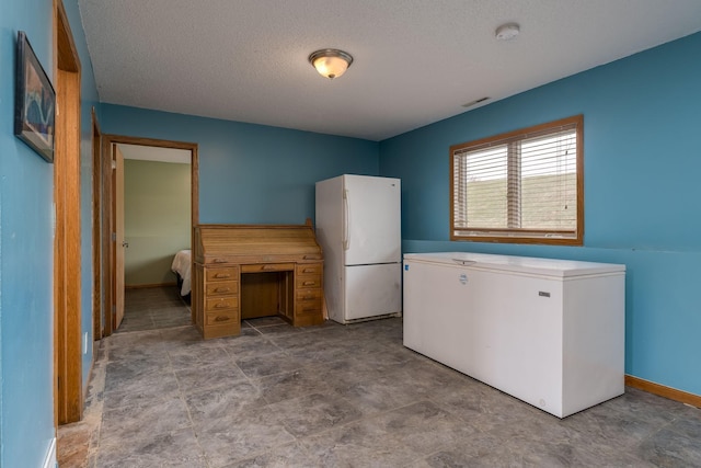 interior space featuring freestanding refrigerator, a textured ceiling, visible vents, baseboards, and fridge