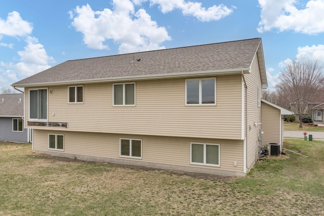 rear view of house with a yard, cooling unit, and a shingled roof
