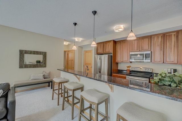 350 Main St N Unit 230, Stillwater, MN 55082 - kitchen featuring stainless steel appliances, a breakfast bar area, dark stone countertops, brown cabinets, and hanging light fixtures