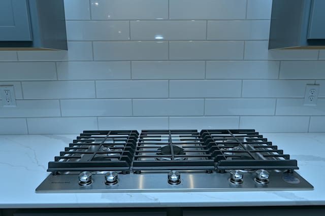 interior details with stainless steel gas stovetop, backsplash, and light stone counters