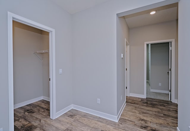unfurnished bedroom with a walk in closet, baseboards, and wood finished floors