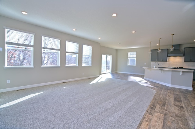 unfurnished living room featuring baseboards, recessed lighting, visible vents, a sink, and wood finished floors
