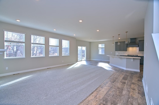unfurnished living room with baseboards, recessed lighting, visible vents, a sink, and wood finished floors
