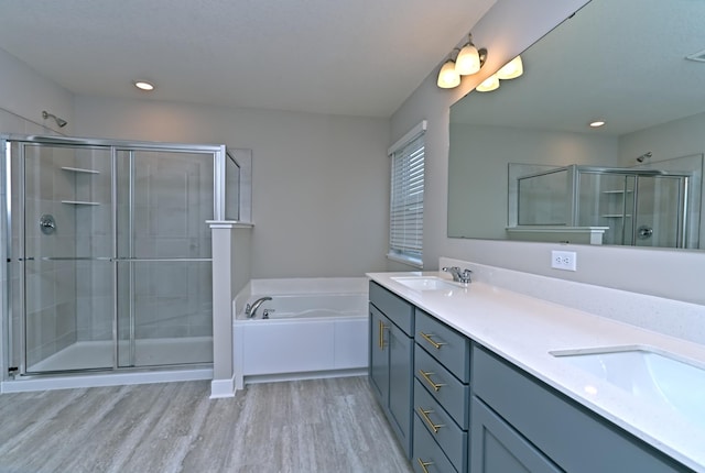 full bathroom featuring double vanity, a shower stall, a bath, a sink, and wood finished floors