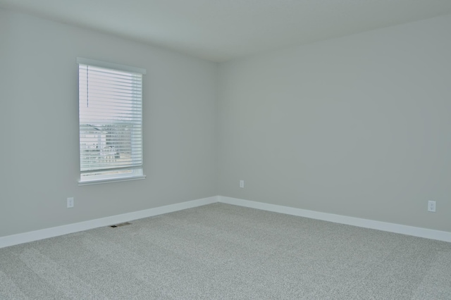 carpeted spare room featuring baseboards, visible vents, and plenty of natural light
