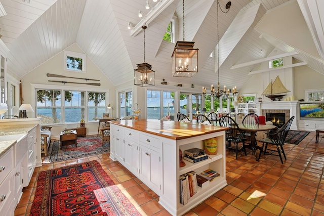 19820 Lakeview Ave, Deephaven, MN 55331 - kitchen featuring wooden counters, a chandelier, a brick fireplace, high vaulted ceiling, and white cabinetry