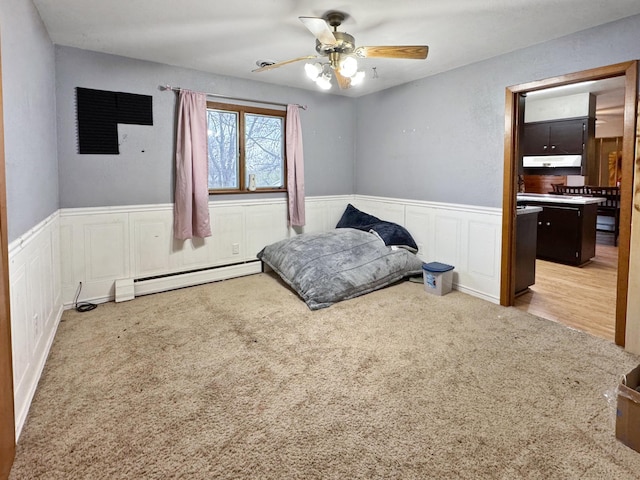 bedroom with a wainscoted wall, baseboard heating, carpet flooring, and a decorative wall