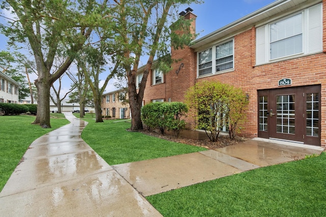 view of property exterior featuring a chimney, brick siding, french doors, and a yard