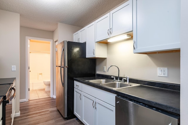 2930 Blaisdell Ave Unit 124, Minneapolis, MN 55408 - kitchen with stainless steel appliances, a sink, white cabinetry, dark countertops, and a textured ceiling