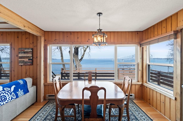 12742 Lake Miltona Dr NE, Miltona, MN 56354 - dining room featuring a water view, wooden walls, light wood-style flooring, a baseboard radiator, and a textured ceiling