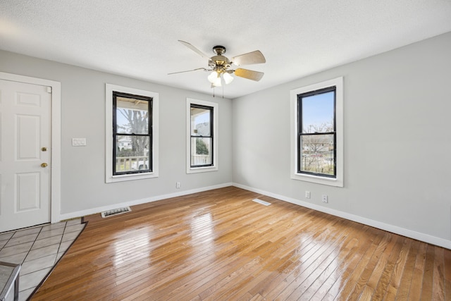 unfurnished room with plenty of natural light, light wood-style flooring, visible vents, and a ceiling fan