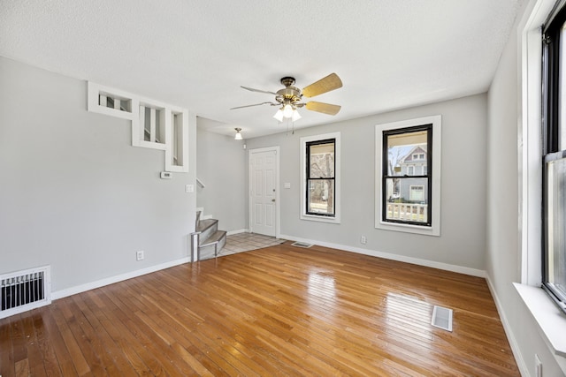 unfurnished room featuring visible vents, hardwood / wood-style flooring, ceiling fan, and stairs