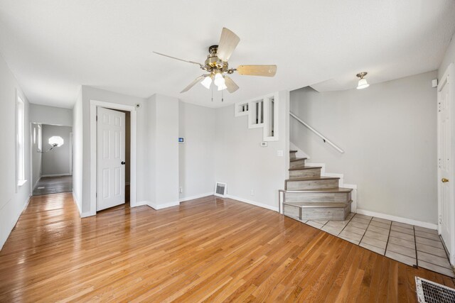 unfurnished living room featuring stairway, visible vents, light wood-style floors, baseboards, and ceiling fan