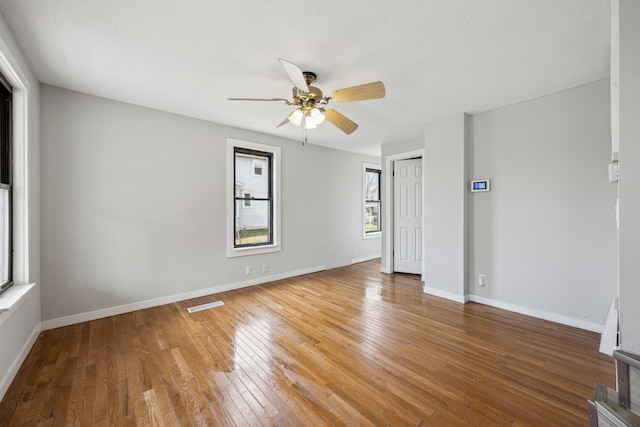 empty room featuring hardwood / wood-style floors, visible vents, a ceiling fan, baseboards, and a textured ceiling