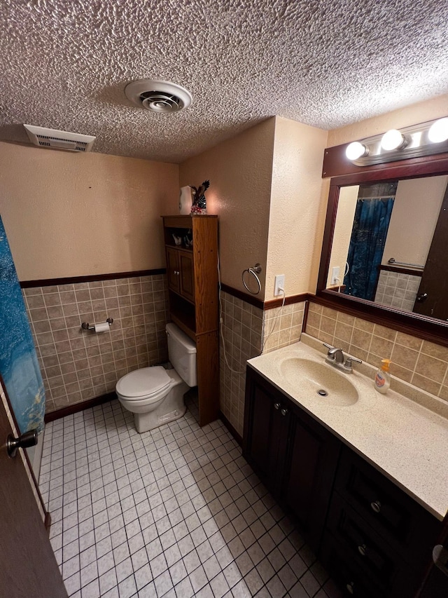 22612 Greenwood Loop, Park Rapids, MN 56470 - bathroom featuring tile walls, a textured ceiling, toilet, vanity, and wainscoting