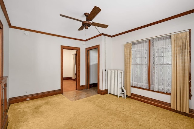 carpeted spare room featuring radiator, a ceiling fan, baseboards, ornamental molding, and a smoke detector