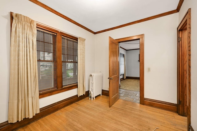 empty room featuring radiator heating unit, crown molding, light wood-style flooring, baseboards, and healthy amount of natural light