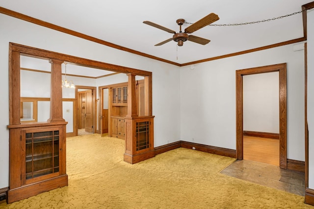 carpeted spare room featuring ceiling fan, crown molding, baseboards, and a chandelier