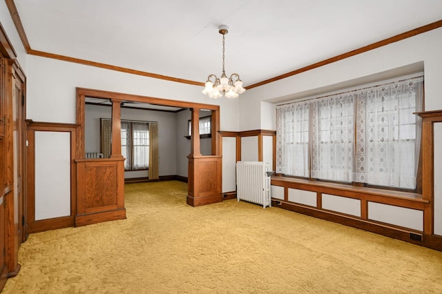 empty room featuring radiator, light colored carpet, crown molding, a chandelier, and baseboards