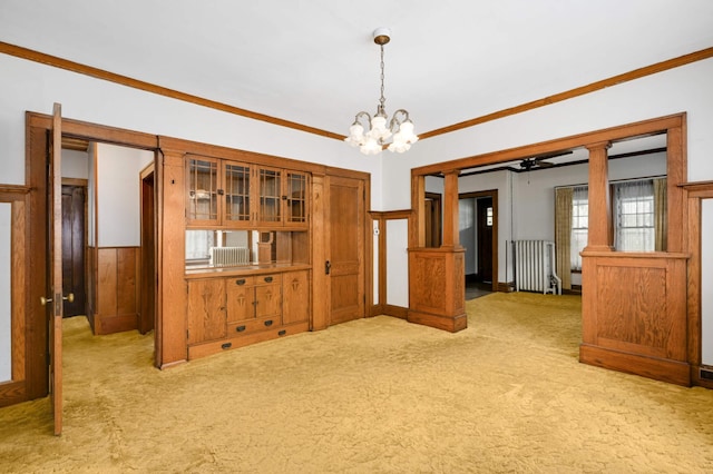 unfurnished dining area featuring radiator, light carpet, a chandelier, ornamental molding, and wainscoting
